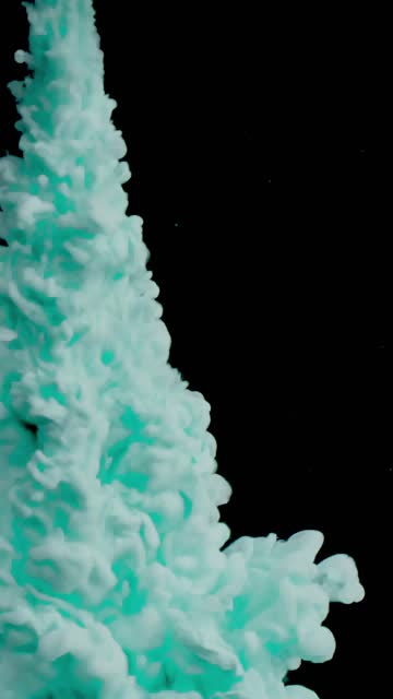 Turquoise colored smoke flow from top to bottom over a black background on a vertical video .