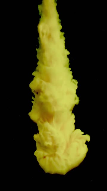 Vertical video of a vibrant yellow substance injected from top to bottom into a black liquid creating a mesmerizing fluid show.