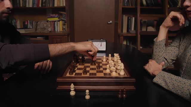 A young couple playing chess surrounded by bookshelves.