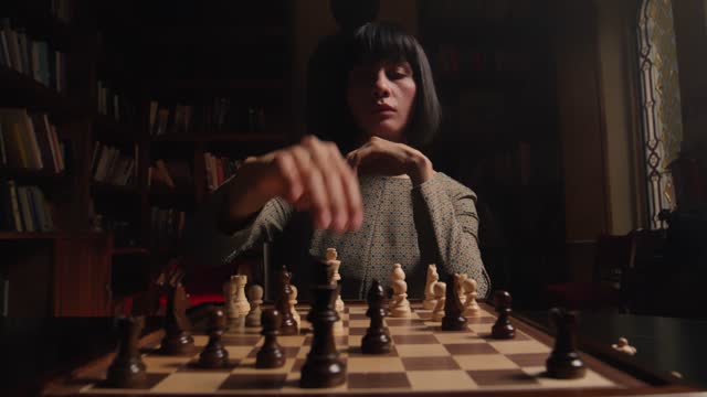 A serious looking woman move a chess piece and waits for her opponent's move.