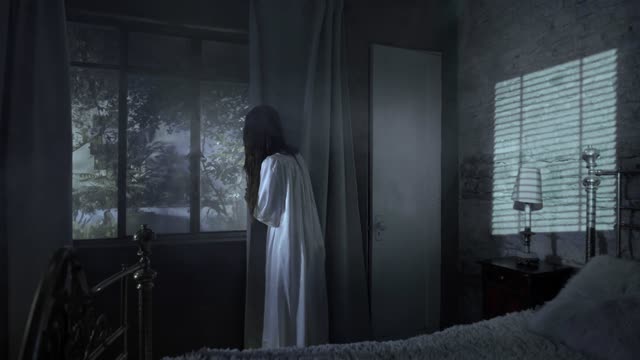 Eerie figure in white gazes out darkened window.