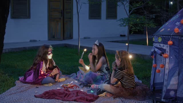 Kids in costumes enjoy a magical night picnic outside.