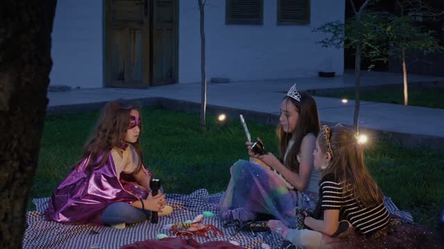 Children in costumes enjoy a nighttime picnic outside.