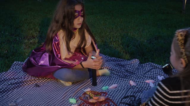 Kids in costumes enjoy a nighttime picnic on a blanket.