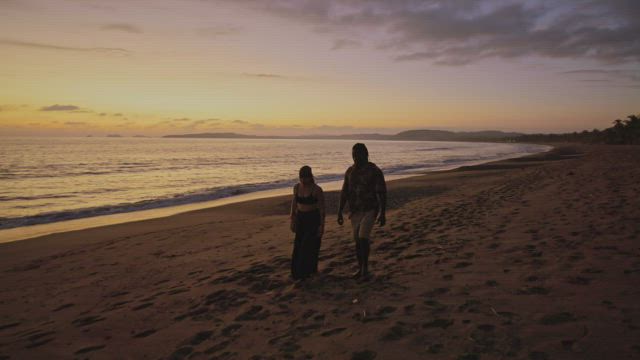 Romantic couple walk along a beach at sunset.