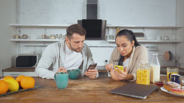 Couple having breakfast cereal and see their cell phones.