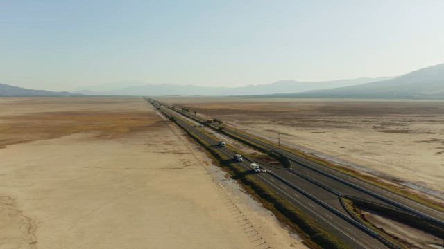 An asphalt road with vehicle traffic traverses the plain desert terrain under the scorching sun.