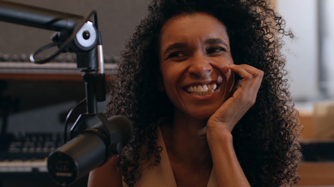 A mature black woman smiling and laughing with joy in front of a podcast microphone.