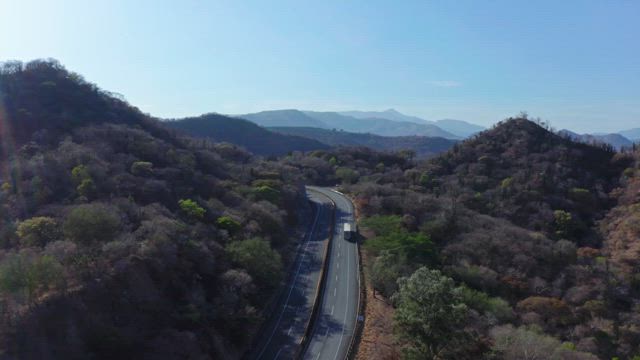 Aerial view of an asphalt road surrounded by the mountains covered in arid vegetation under the clear blue sky.