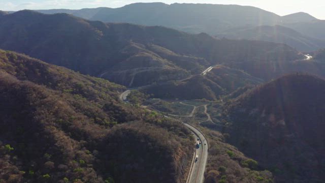 Flying over a rugged landscape with a w highway traversing the mountains at dusk.