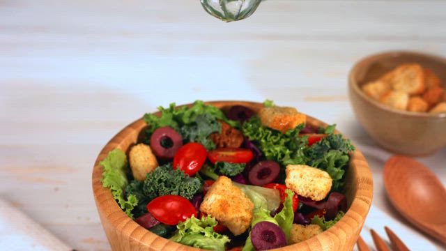 Olive oil pours down into a delicious fresh salad on a rustic wooden bowl on the table.