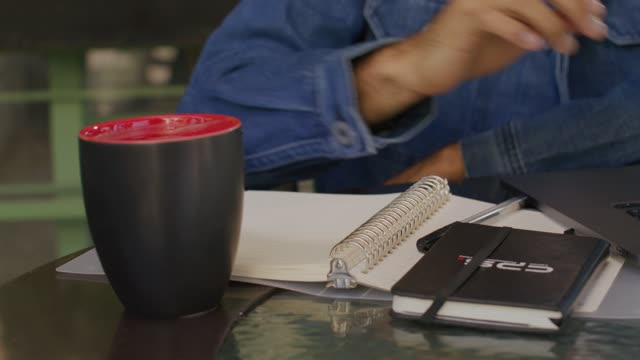 A young man wearing a blue denim jacket and headphones takes a sip from the black coffee cup.