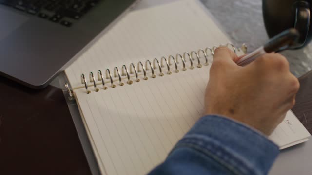 Close up a hand writing notes on a notebook with a pen.