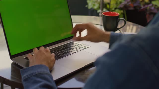 A young business man working on a laptop on the table takes a sip of coffee.