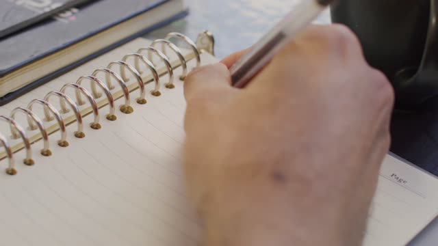 Close up of a hand writing to do list on a yellow paper notebook.