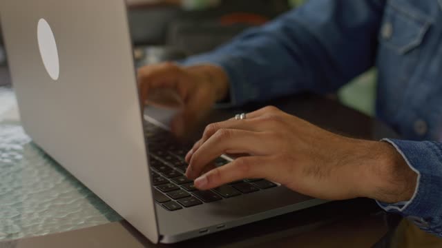 Skillful male hands adorned with rings typing on a laptop.