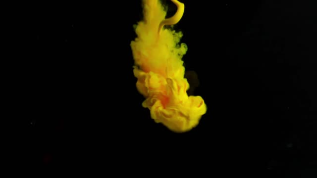 A vibrant yellow and pink substance, likely smoke or ink, dispersing in water. The fluid forms intricate, organic patterns as it moves, creating a visually captivating scene.