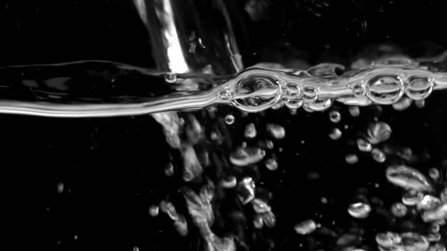 Over a black backdrop a stream of water create a mesmerizing spectacle of bubbles.