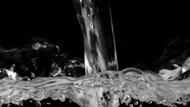 A stream of transparent water fills a container over a black background.