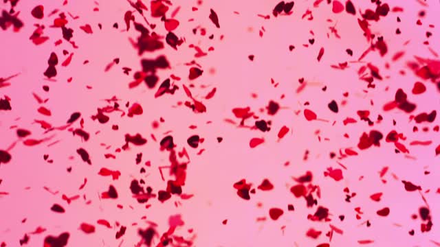 Metallic heart shaped confetti falling in slow motion over a pink background.