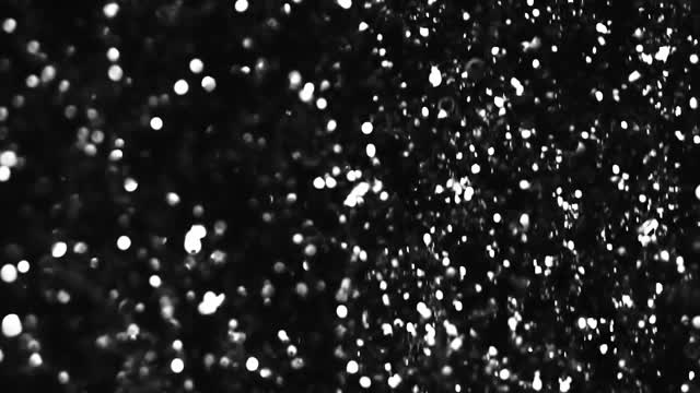 Shimmering silver confetti falling down over a black background.