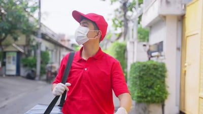 Asian delivery man in red uniform with face mask carrying bag of food delivering food to customer..