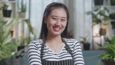 Close Up Of Asian Woman With Plants Crossing Her Arms And Smiling To Camera At Home.