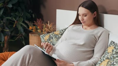 Closeup Shot of a Pregnant Woman's Hands Holding a Tablet Swiping and Observing Photos with a Hint.