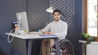 Disabled man works in the office and looks at the camera, smiling..