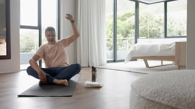 Relaxed senior biracial man practicing yoga sitting floor at home, copy space, slow motion.